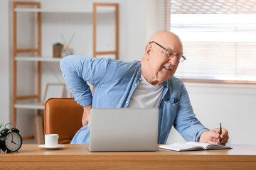Senior man with back pain writing in notebook at table