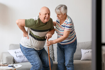 Senior woman and her husband with walking stick suffering from back pain at home