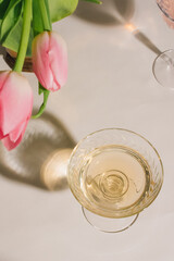 pink tulips with white wine in coupe glass on white background