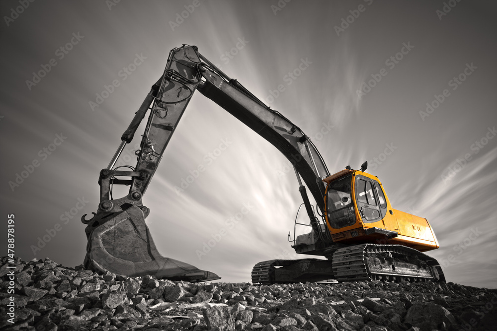 Wall mural excavator parked on stone ground against dramatic sky