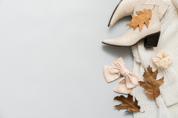 Stylish female shoes, sweater, scrunchy, hair bow and autumn leaves on light background