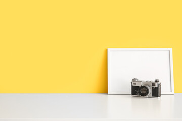 Blank photo frame and vintage camera on table near color wall