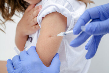 Criança tomando vacina no braço com prevenção do covid 19 e medico com luva azul e seringa na mão.