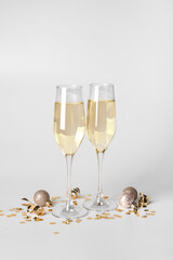 Glasses of champagne with Christmas balls and confetti on white background