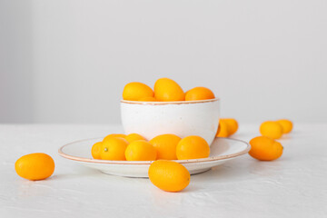 Bowl with tasty kumquat fruits on light background