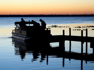 Silhouette of Three Retired Men Heading Out for a Day of Fishing in Their Pontoon Boat at Sunrise - 478881356