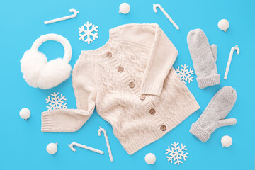 Stylish sweater, mittens, ear muffs and winter decor on blue background