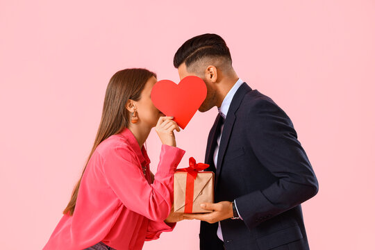 Happy young couple with gift and red heart on color background. Valentine's Day celebration