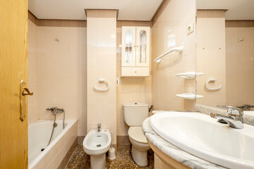 Fototapeta na wymiar Conventional toilet with white bidet and fixtures and cream-toned walls