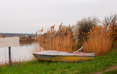 A boat on a lake in Pavlovka fishing resort not far from Odessa, Ukraine. Yellow dry reeds, blooming spring tree, calm atmosphere.