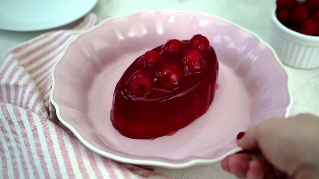 Slow motion food footage. Pink red jelly with fruit wobbles on a pale pink dish. Fruit, kitchenware and napkin included in frame. Pastel pink and red colour theme.