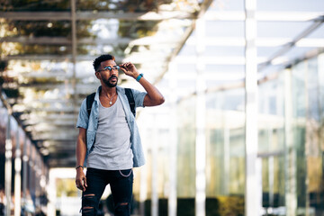 Black man with glasses and backpack walking down the street. Picking up his glasses with his hand.