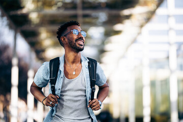 Happy and smiling black man with glasses and backpack walking down the street. Taking the handles...