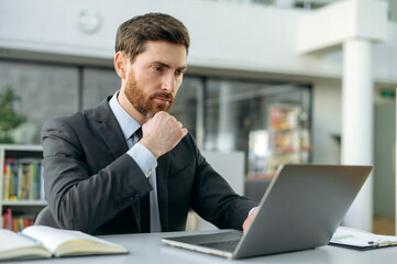 Fototapeta na wymiar Concentrated serious attractive caucasian businessman, ceo, financial expert, sitting in a modern office, uses a laptop, analyzes, develops a startup, plans a financial business strategy, thinking