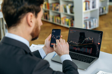 Exchange market. Smart man investor and crypto trader, using laptop and cellphone, analyzes charts of trading in stock market and digital cryptocurrency exchange,conducts analysis,trading crypto coins