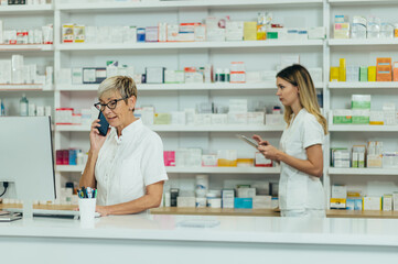 Obraz premium Senior female pharmacist working in a pharmacy with her young colleague