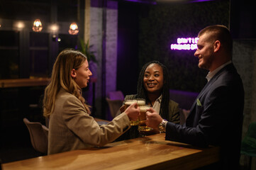 Cheerful colleagues drinking beer in the bar together after work and using a tablet