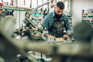 Male worker pressing ink on frame while using the printing machine in a workshop