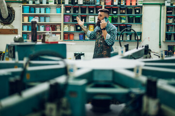 Male worker mixing colors for screen printing in a workshop and using a smartphone