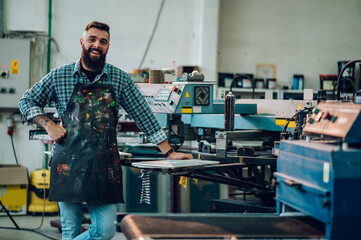 Male worker posing while using printing machine in a workshop