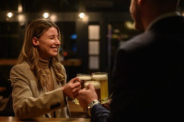 Cheerful colleagues drinking beer in the bar together after work and using a tablet