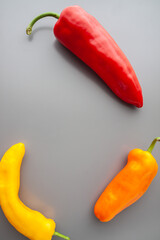 Three colourful oblong paprikas on the gray background. Top view. Vegetarian. Copy-space. Healthy food and living. Vertical.