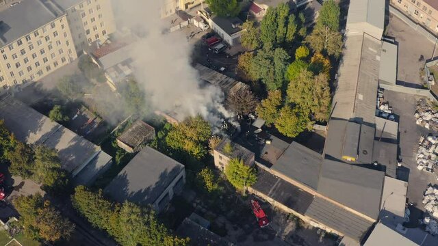 The fire brigade extinguishes the flames of a fire in an industrial warehouse. Team 911 extinguishes a fire from the arson of a warehouse in the city in the afternoon - an aerial drone shot.