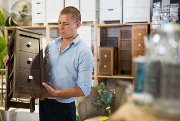 Portrait of positive man choosing dressing table in furniture store