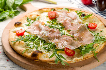 Pizza with Parma ham and arugula and tomatoes on the board macro close up on white wooden table, primavera