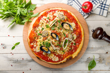 Pizza with seafood, cheese and tomato sauce on wooden board top view on white wooden table