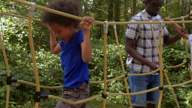 A father with his children plays on the forest playground, helps them train their agility on the rope road. Physical development is the most readily visible of the child development domains. 