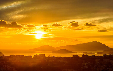 View of sunset above the gulf Naples from San Elmo castle: yellow sky with clouds, mountains, city buildings