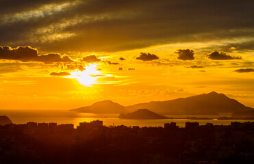 View of sunset above the gulf Naples from San Elmo castle: yellow sky with clouds, mountains, city buildings