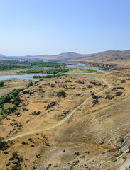 View from Cave City at Uplistsikhe. Mtkvari river, dry yellow grass, meandering ground road, green trees, blue sky, hills on the horizon