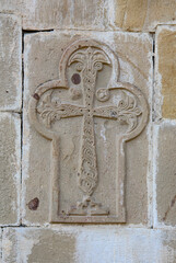 Carved stone cross on the wall of the Dormition of the Virgin Mary church in Ananuri fortress in Georgia. Blue sky, sunlight and shadows on the ancient stones