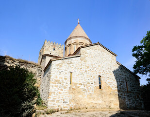 Obraz premium Ananuri church and fortress in Georgia. Blue sky, grenn trees, narrow windows, sunlight and shadows on the ancient stones