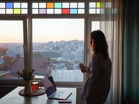 Woman with a coffee looking to the window at evening