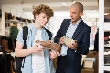 Fototapeta na wymiar Man visiting shoe shop with teenage son in search of comfortable elegant formal shoes .
