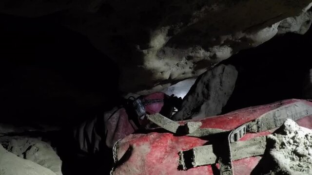 Dusty female caver passes gear bags down narrow vertical passage
