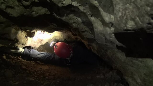 Caver in red helmet pulls himself through rock restriction in darkness