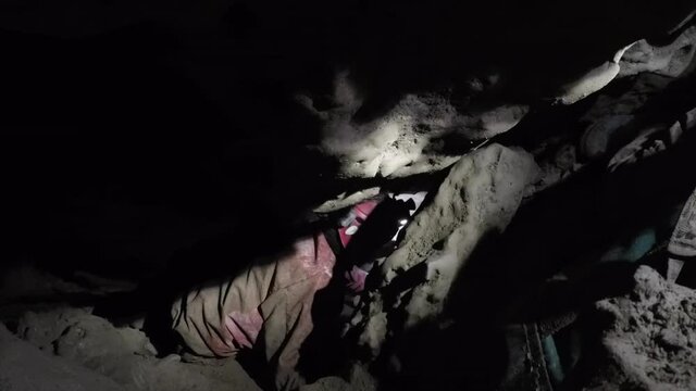 Female expedition caver passes gear bags down steep tight passage