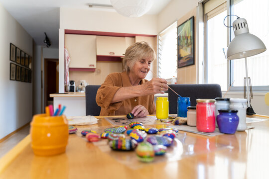 Senior woman painting mandalas on stones at home