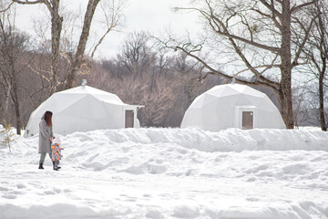 Mom and little daughter are walking through winter glamping.