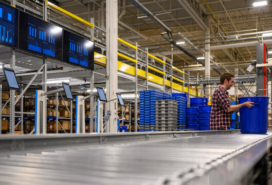 worker grabs barrel  on conveyor belt in warehouse 