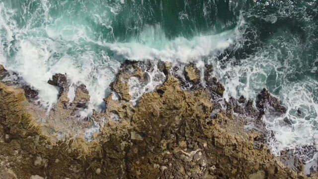 Dolly aerial footage captured by drone over porous limestone rock continuously pounded by the strong ocean waves off the shore of Cozumel, Mexico.