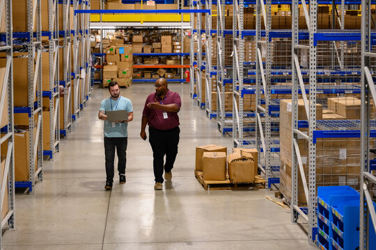 Manager walking with employee in organized warehouse 