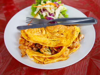 Stuffed Thai Omelette with meat and vegetables on white plate, fork and spoon - obrazy, fototapety, plakaty