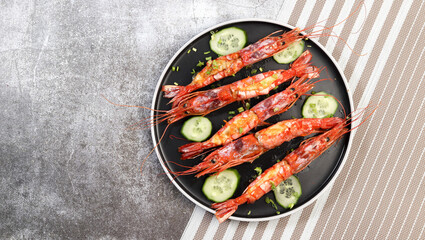 Oven baked Argentinian red prawns stuffed with cheese on a round plate on a dark gray background. Top view, flat lay