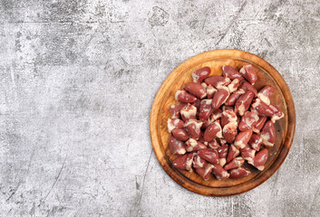 Raw chicken hearts on a round wooden cutting board on a dark grey background. Top view, flat lay