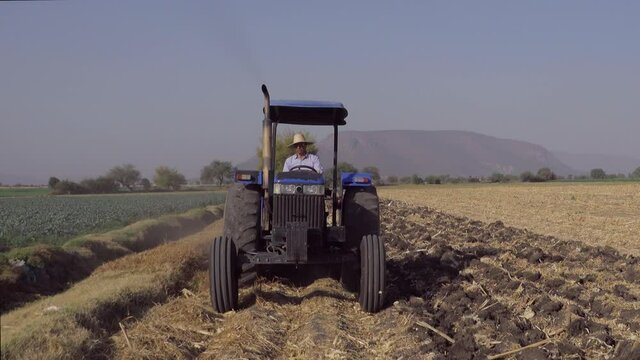 Front view of a real farmer plowing the field with his tractor, preparing the soil to plant new seeds